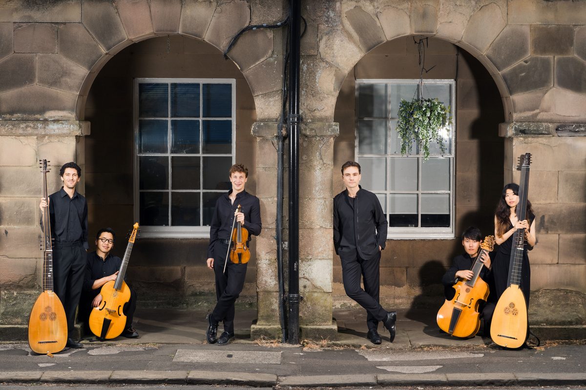 The ensemble spread beneath two stone arches at dusk, instruments in hand