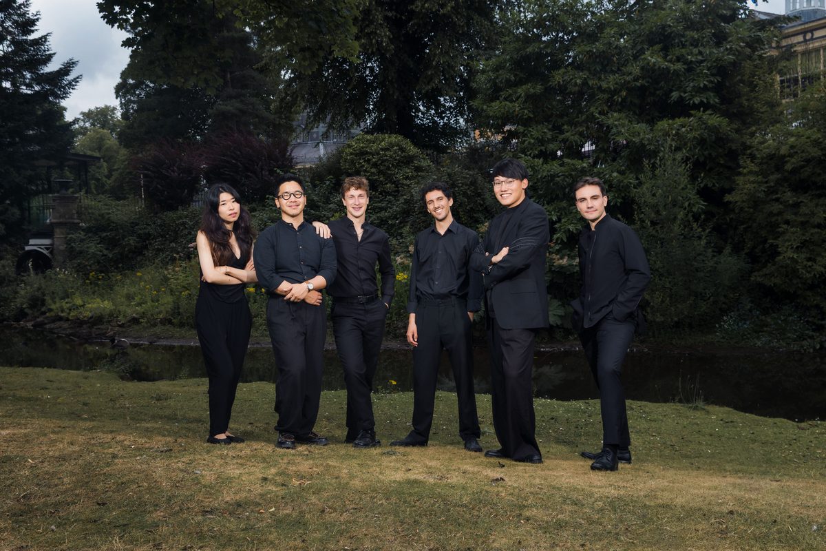 The ensemble standing together on parkland grass at dusk