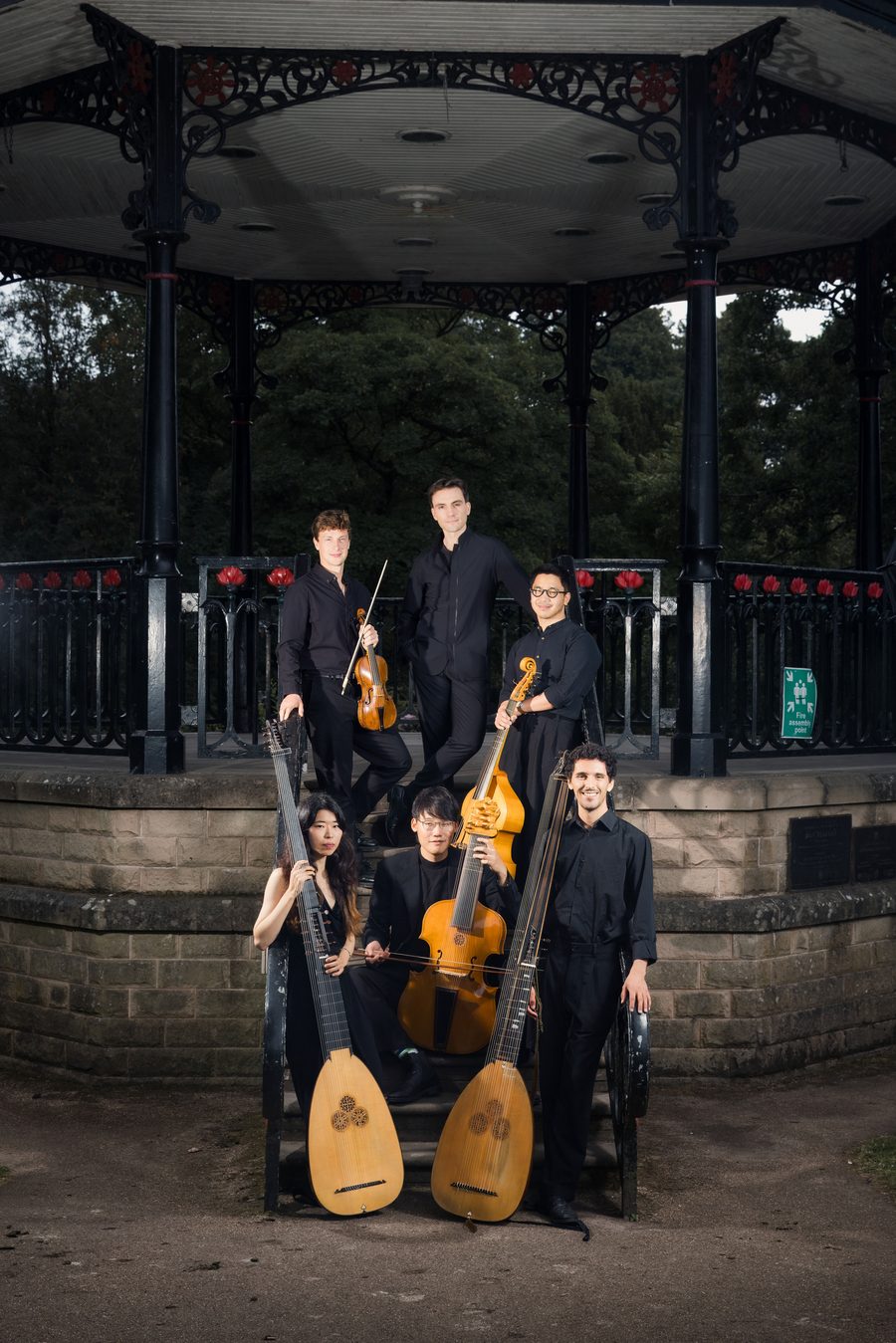 The six musicians of Música d'Outrora posed with theorbo, archlute, viol and violin on the steps of a Victorian bandstand