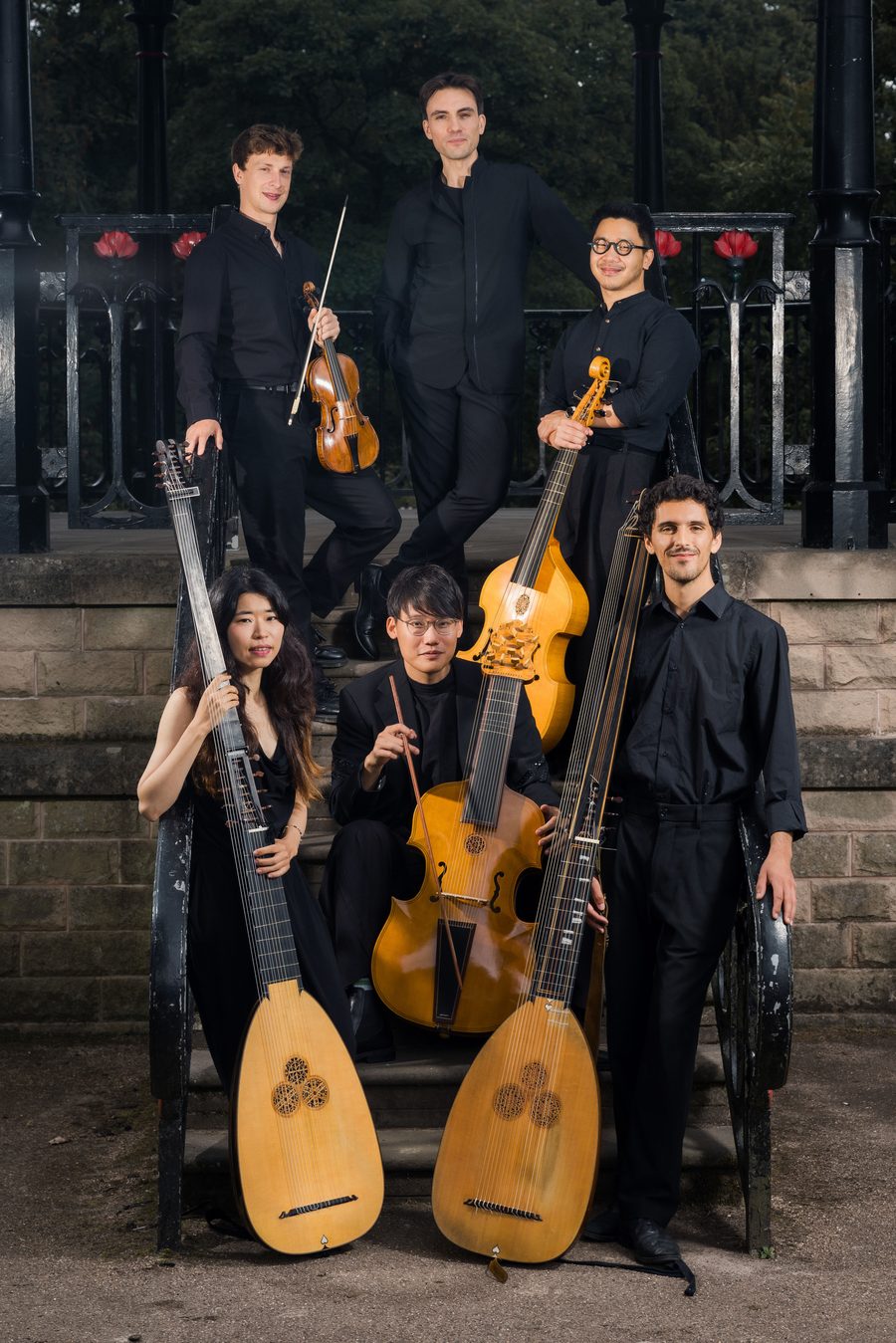 The six musicians of Música d'Outrora gathered with theorbo, archlute, viol and violin against the wrought iron of a Victorian bandstand